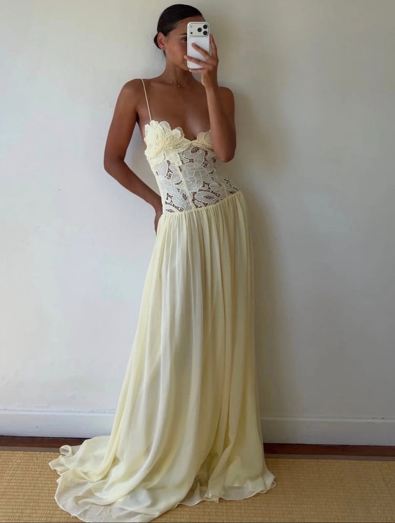 Woman wearing a long, light-colored dress with lace detailing against a plain wall.