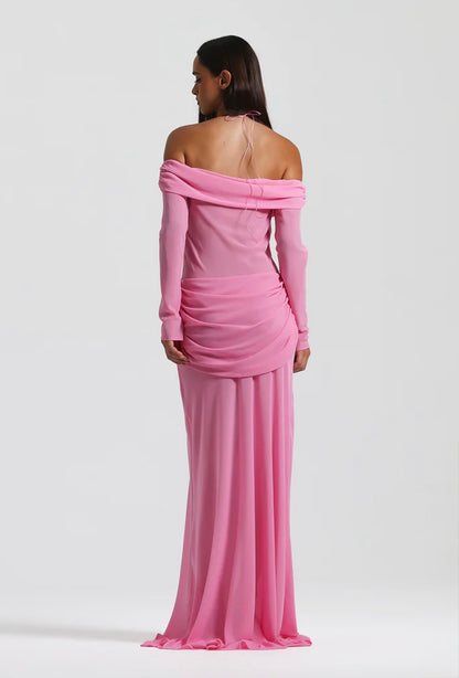 A woman modeling a long-sleeve off-the-shoulder pink gown from the back, shown against a plain light gray studio background.