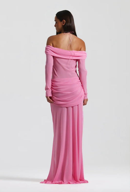 A woman modeling a long-sleeve off-the-shoulder pink gown from the back, shown against a plain light gray studio background.