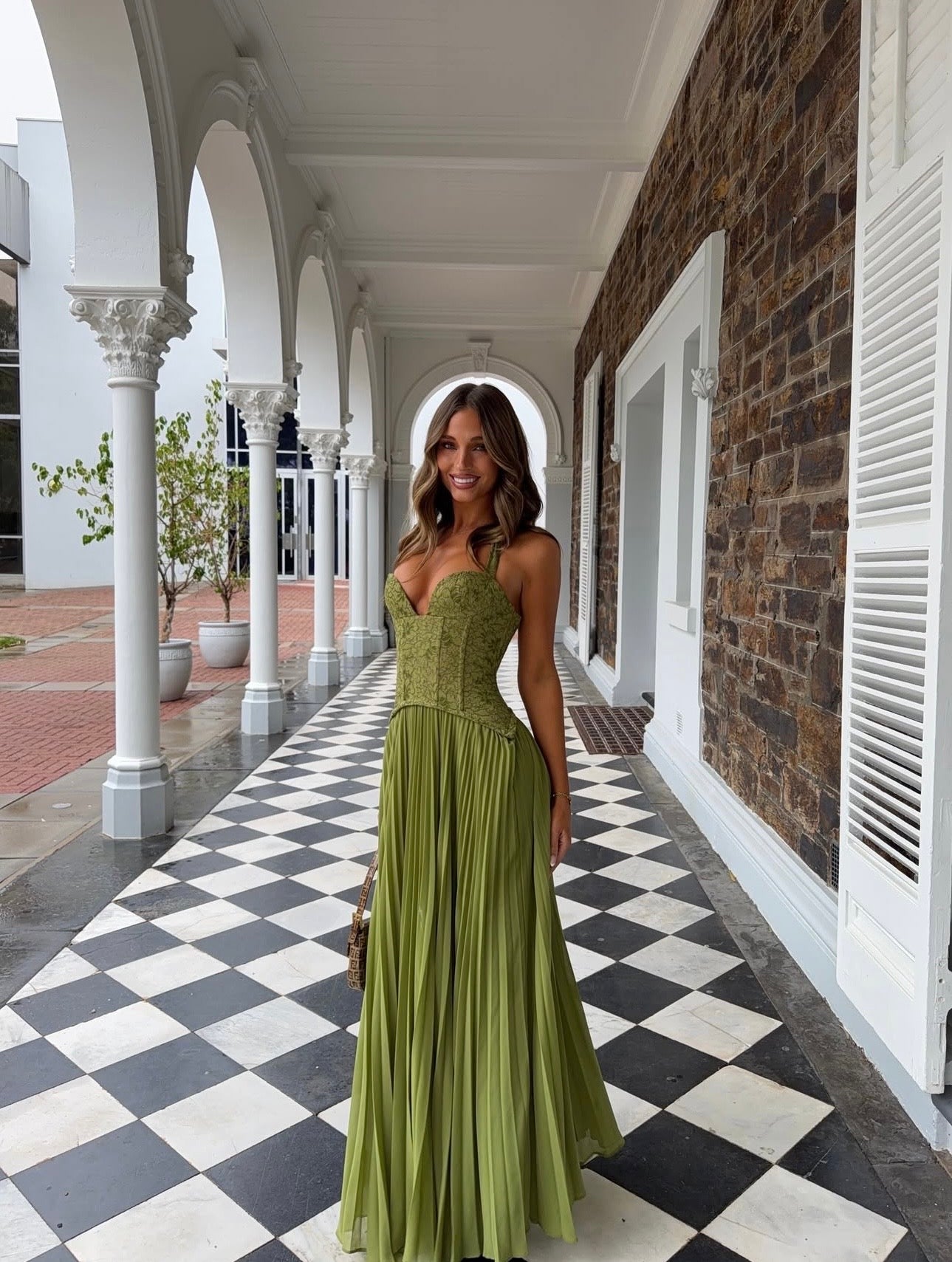 A woman wearing a sleeveless olive green maxi dress with a fitted lace-embroidered bodice .