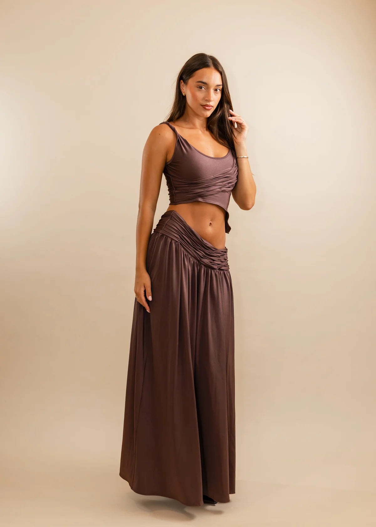 Woman wearing a brown top and long skirt against a beige background