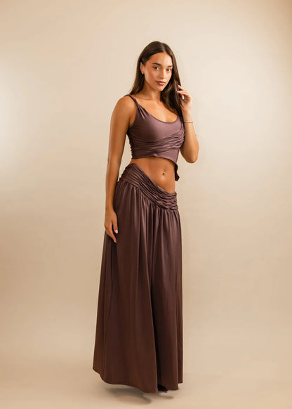 Woman wearing a brown top and long skirt against a beige background