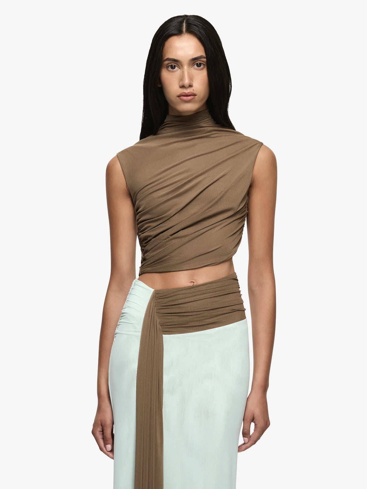 A model wearing a brown draped sleeveless mock-neck crop top and a mint green skirt with a brown waistband, shot against a light gray studio background.