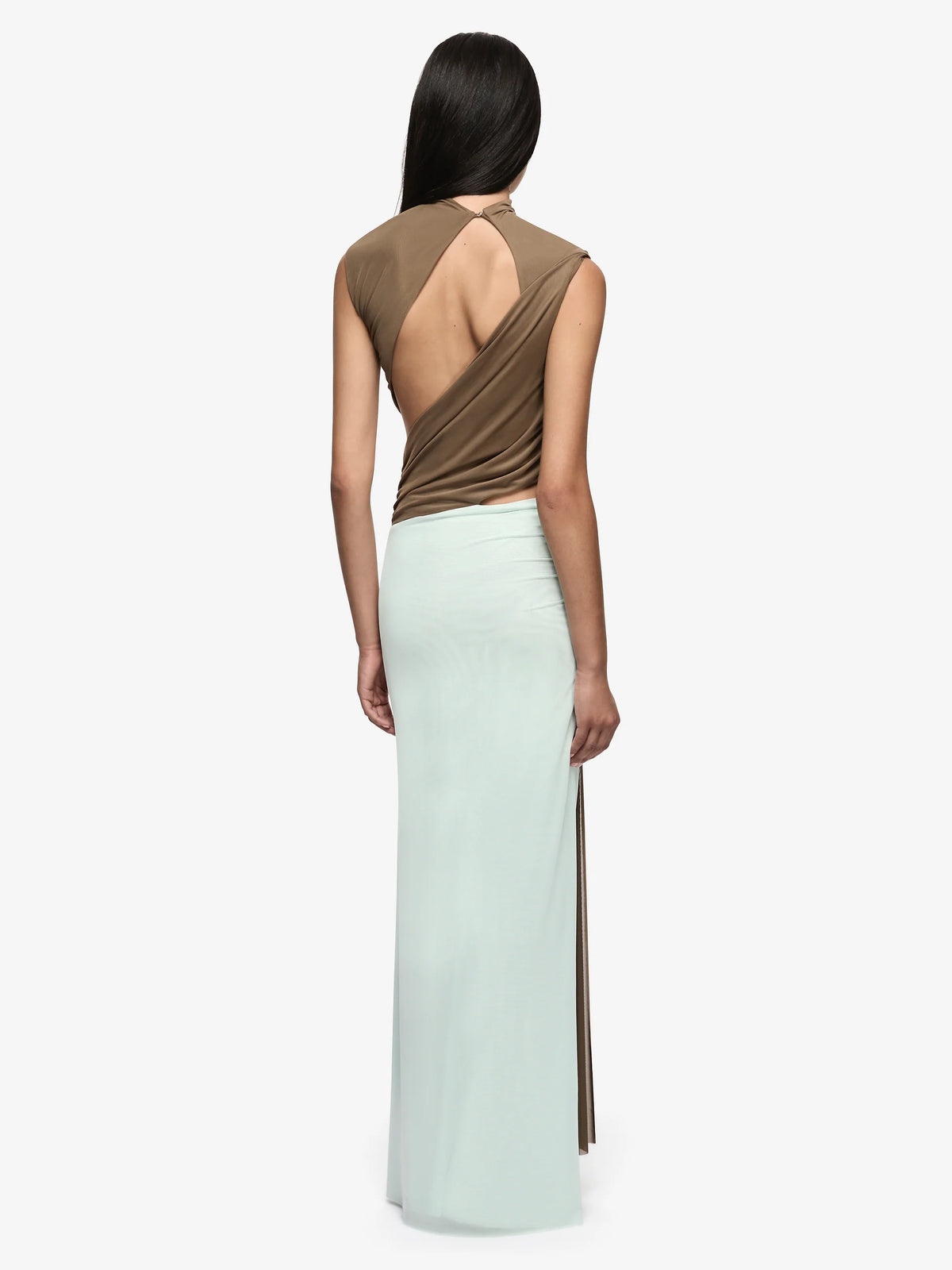 A model shown from the back wearing a sleeveless maxi dress with a draped brown back and a long mint green skirt with side slits, against a plain light gray background.