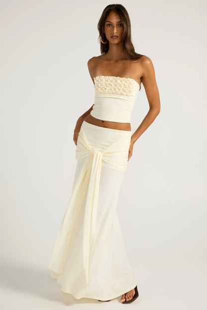 A woman modeling a two-piece cream/off-white outfit consisting of a strapless cropped top .