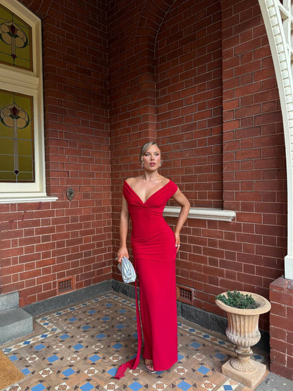 Woman in a red dress standing in front of a brick wall with a decorative plant and window.