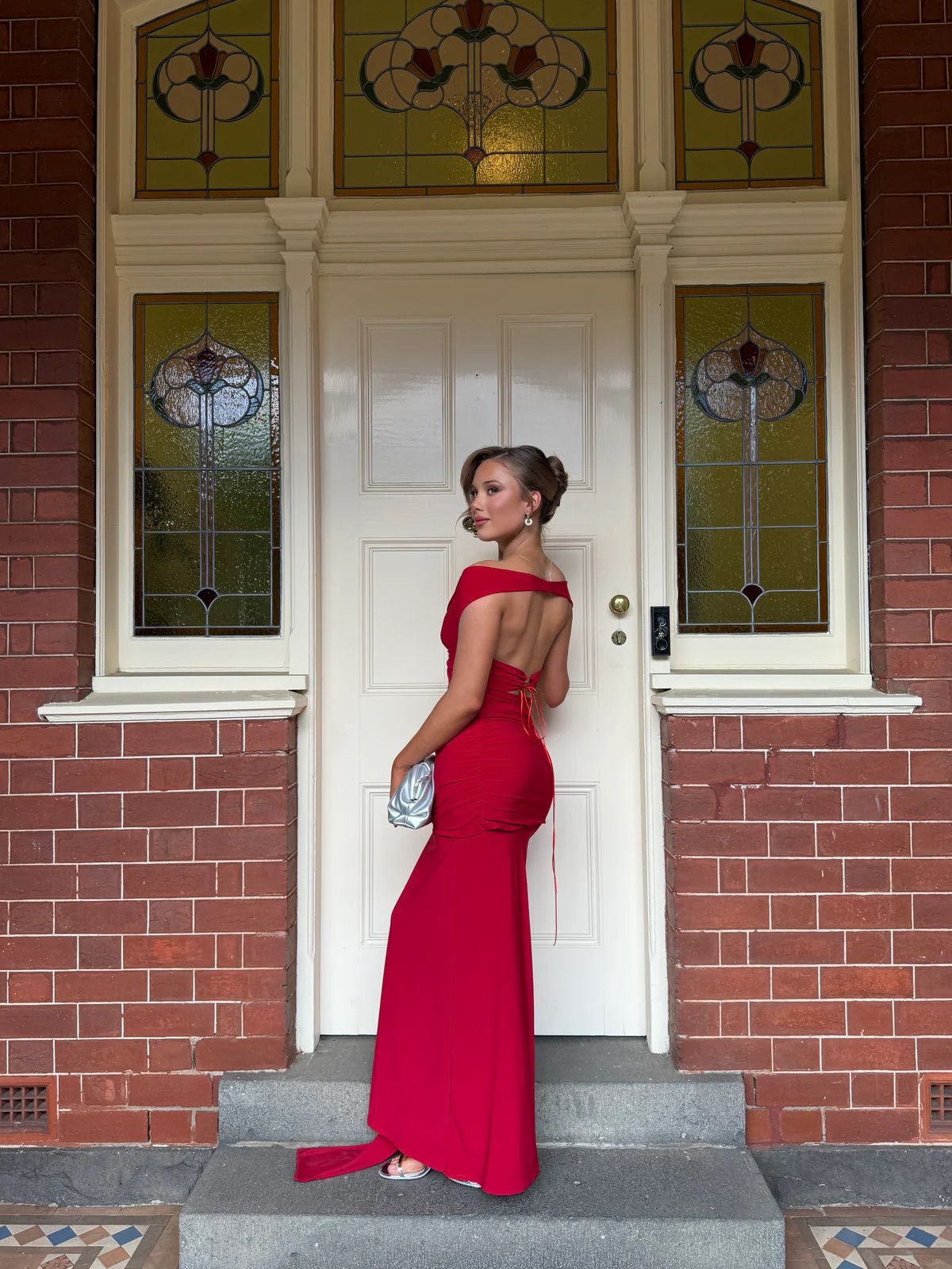 Woman in a red dress standing in front of a brick building with a white door.