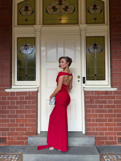 Woman in a red dress standing in front of a brick building with a white door.