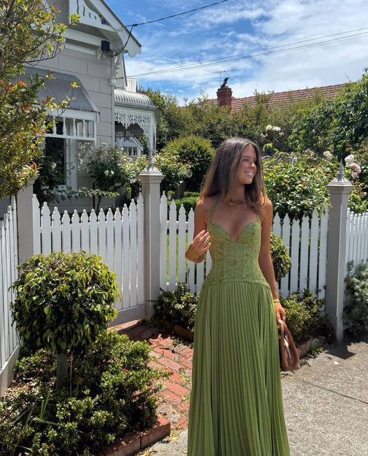 Woman in a green dress standing in front of a white picket fence with a house and garden in the background.