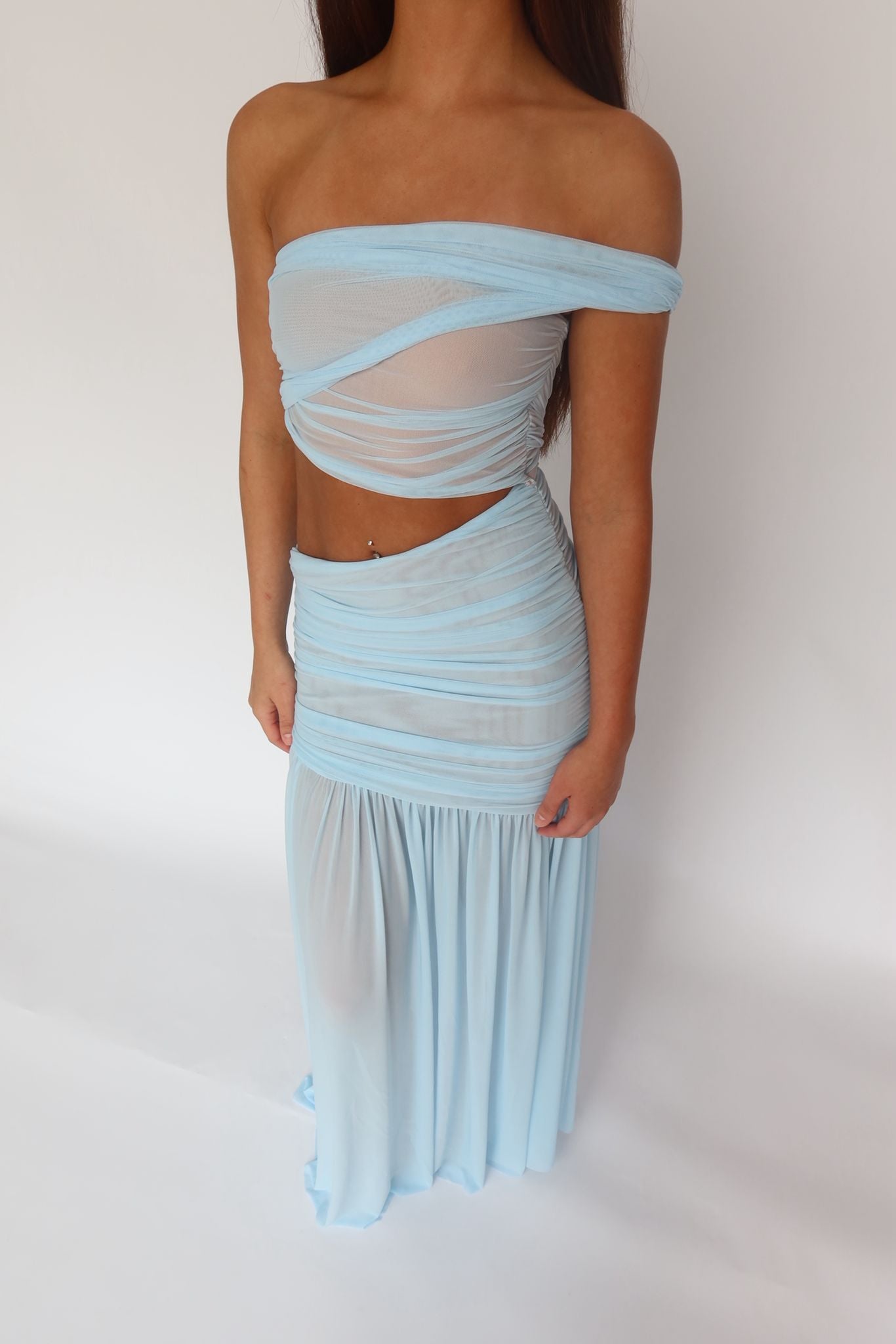 A woman modeling a light blue two-piece sheer mesh set consisting of an off-the-shoulder bandeau top and a matching ruched maxi skirt, set against a plain white studio background.