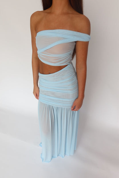 A woman modeling a light blue two-piece sheer mesh set consisting of an off-the-shoulder bandeau top and a matching ruched maxi skirt, set against a plain white studio background.